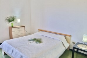 A single bed with a wooden headboard, a bedside table with a lamp, and a small drawer unit.