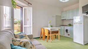 Un espace de vie compact comprenant un canapé, une table à manger et un coin cuisine équipé d’un lave-linge et d’un réfrigérateur.