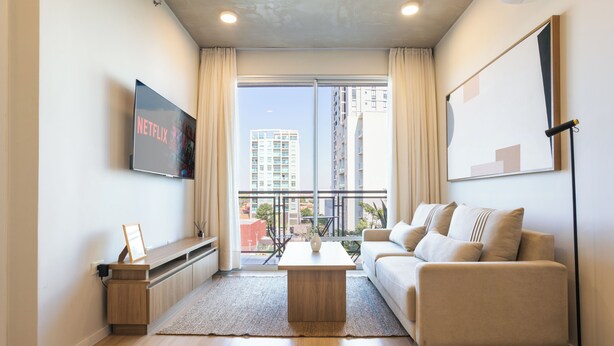 A modern living room with a flat-screen TV, a sofa, a coffee table, and a large window with curtains. - Sky Stays at Life Mariscal (Asunción)