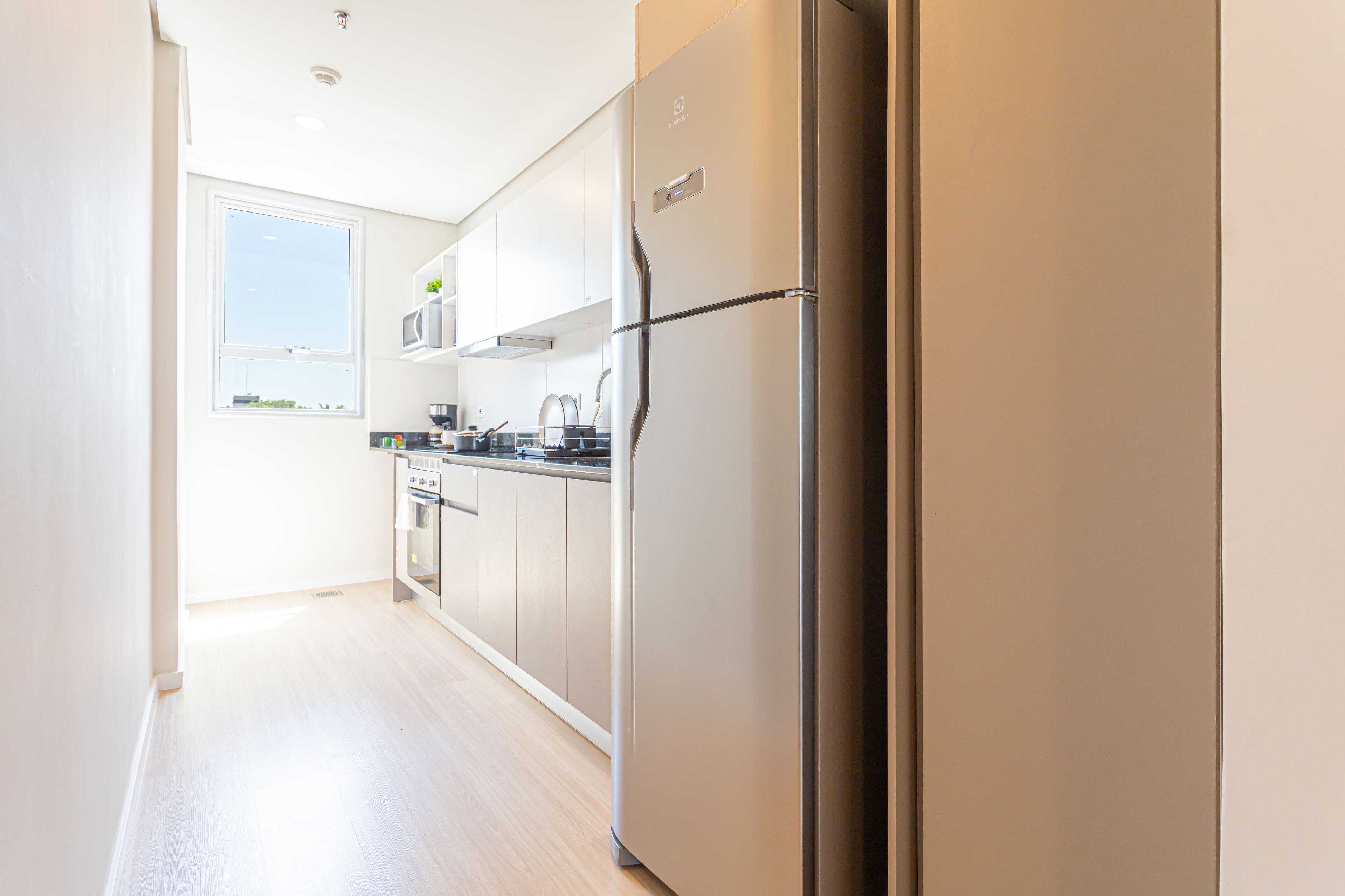 A modern kitchen with stainless steel appliances, white cabinetry, and a large window providing natural light.