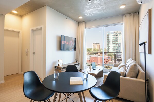 A modern living room with a round table, two chairs, a sofa, and a TV mounted on the wall. - Sky Stays at Life Mariscal (Asunción)
