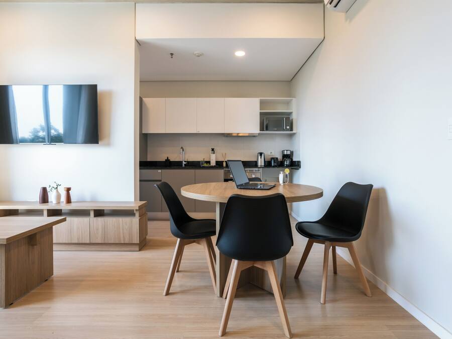 Una cocina moderna con armarios blancos, un microondas y una cafetera. Hay una mesa de comedor redonda con sillas negras y una computadora portátil encima.
