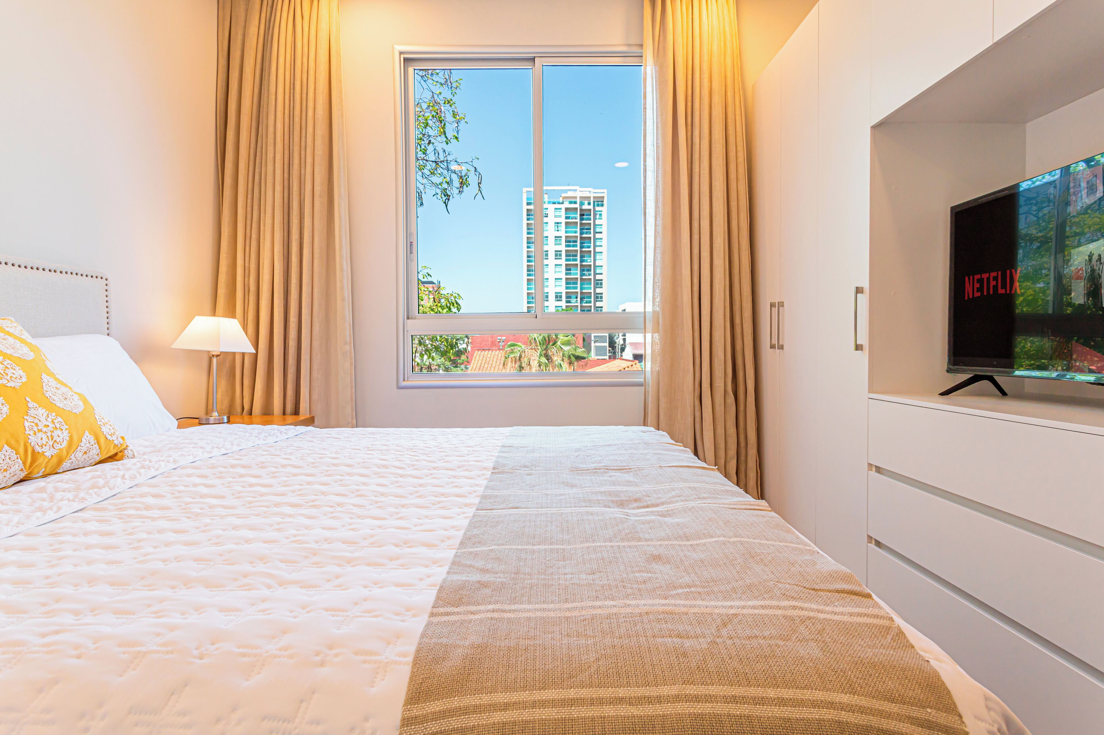 A hotel room with a bed, a TV, and a window with curtains.