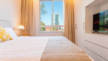 A hotel room with a bed, a TV, and a window with curtains.