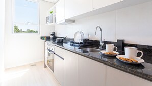 A modern kitchen with white cabinets, a black countertop, a stainless steel sink, and a window providing natural light. - Sky Stays at Life Mariscal (Asunción)