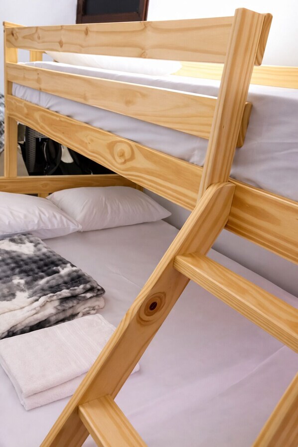 Una cama litera con estructura de madera, ropa de cama blanca y una manta doblada en la litera inferior.