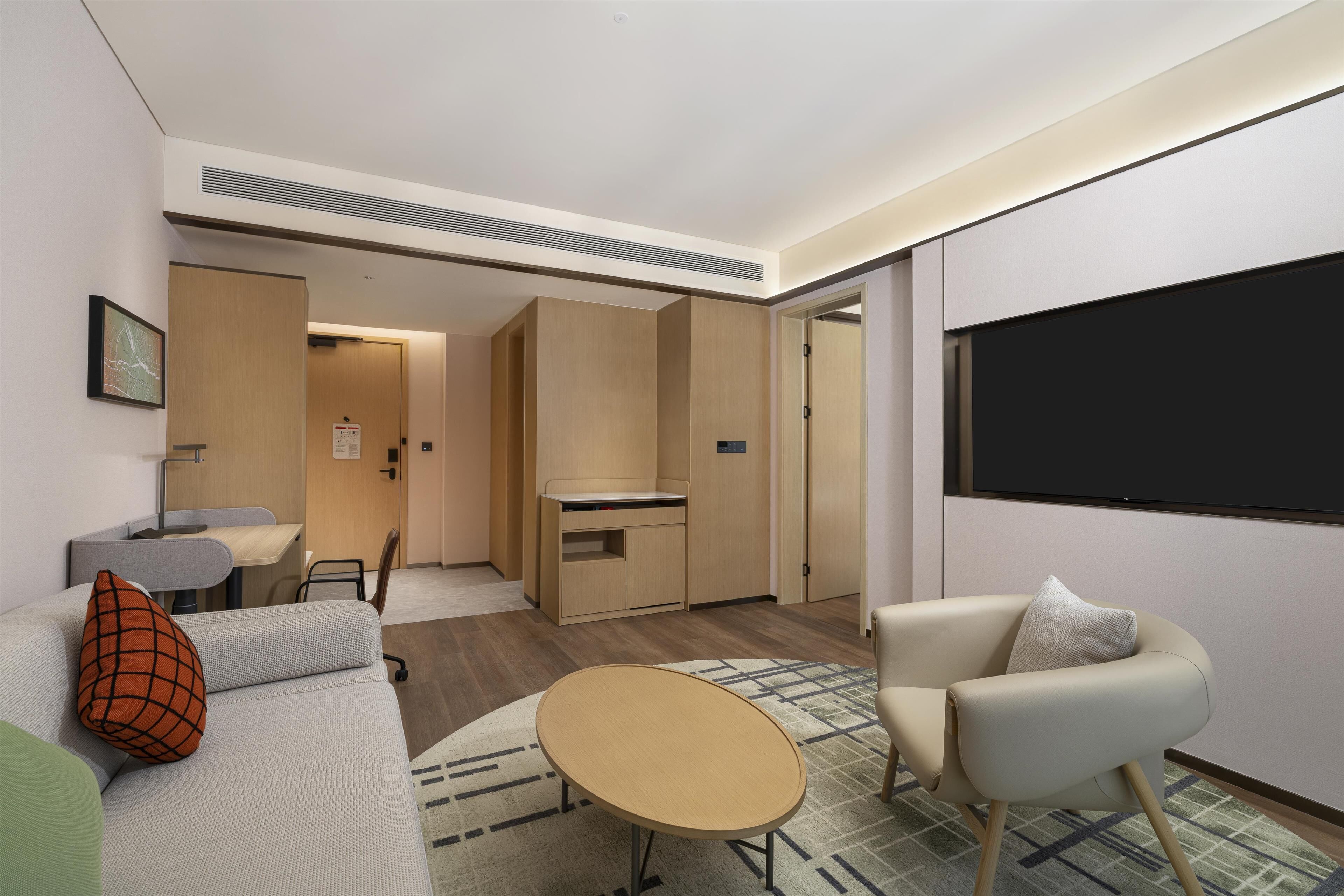 A modern hotel room with a sofa, armchair, small table, and a TV.