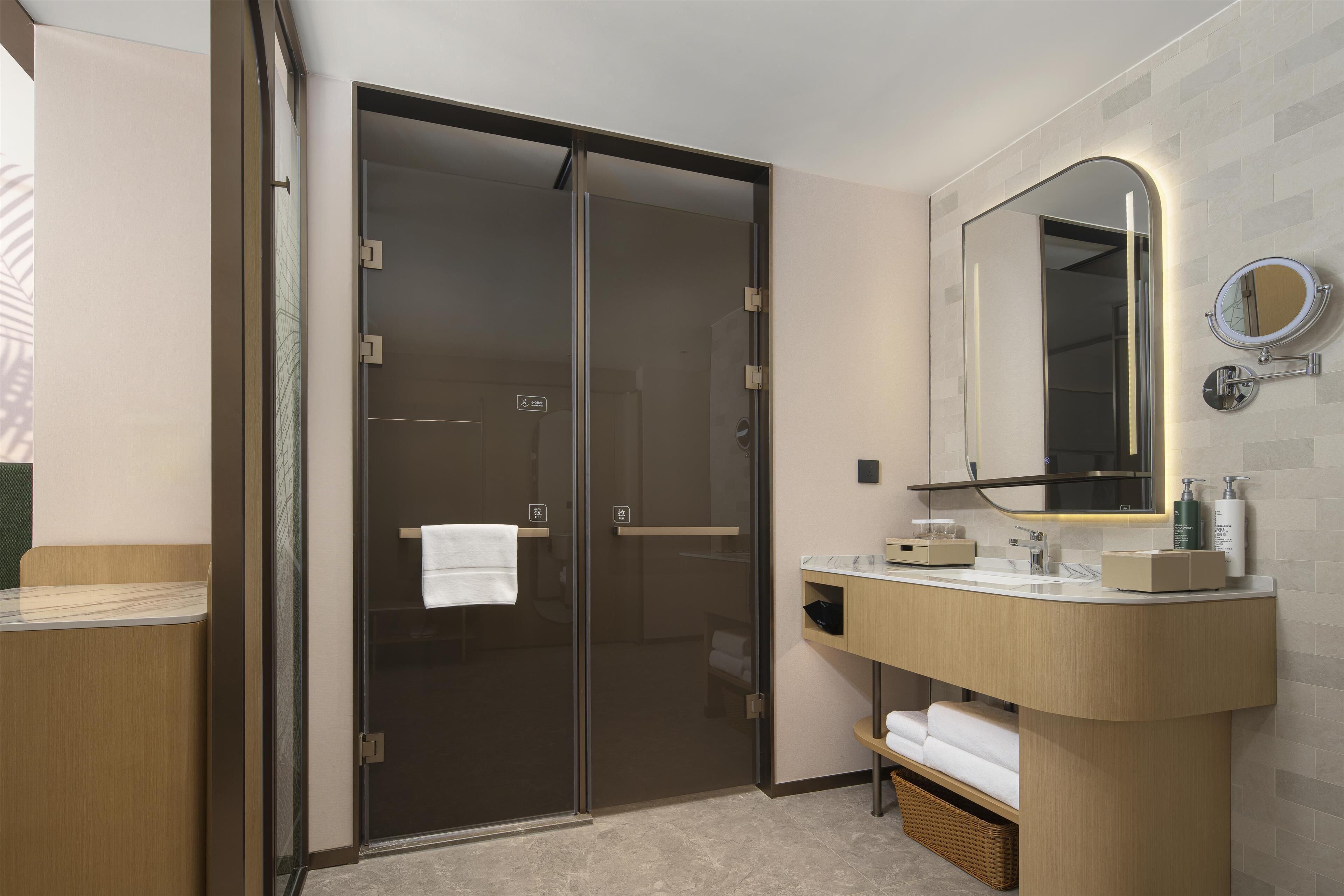 A modern bathroom with a glass shower enclosure, a wooden vanity with a mirror, and a towel rack.