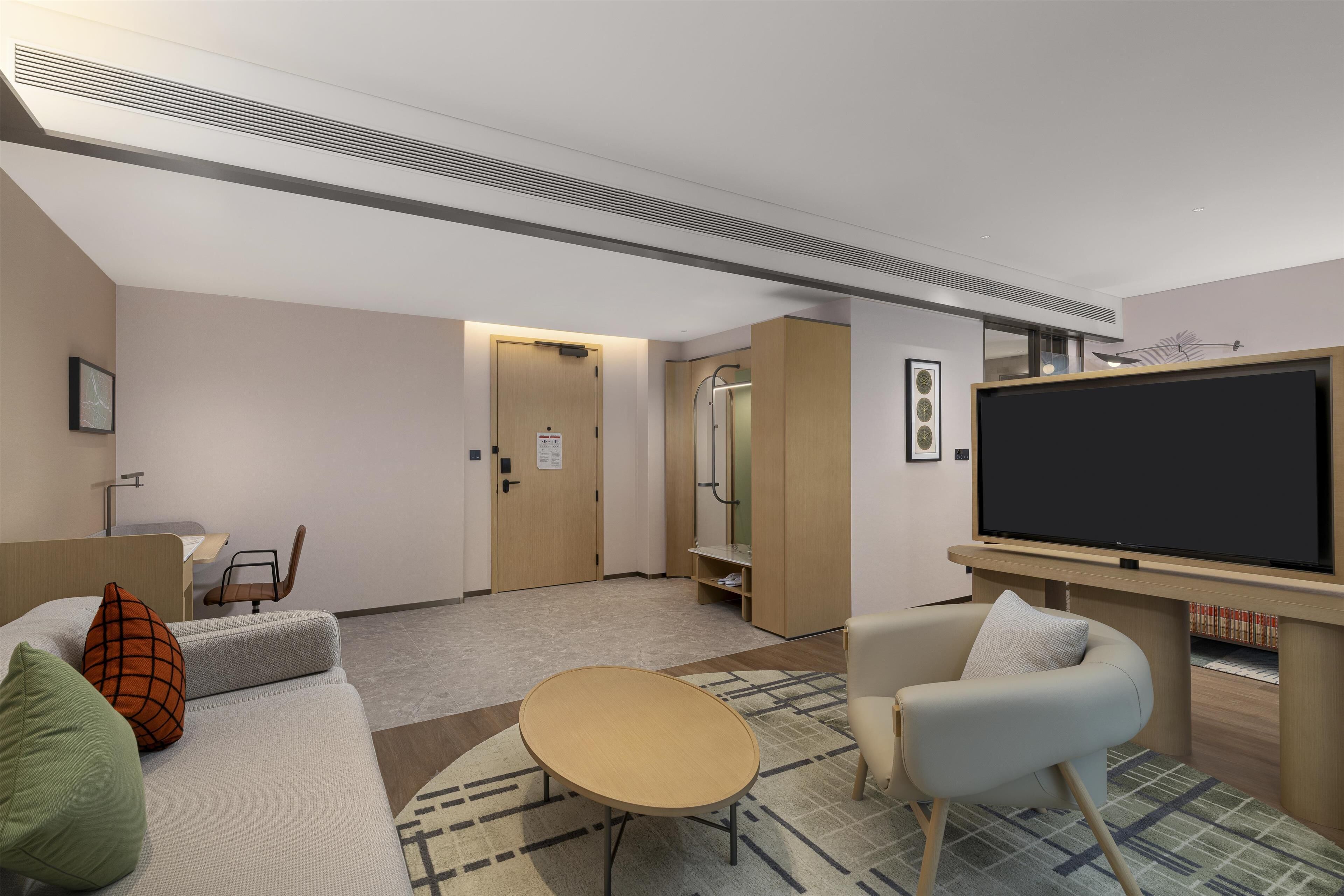 A modern hotel room with a sofa, armchair, TV, and a small table.
