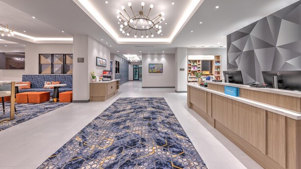 A modern hotel lobby with a reception desk, seating area, and a large patterned rug. - Hampton Inn & Suites Irving Hwy 183 (Irving)