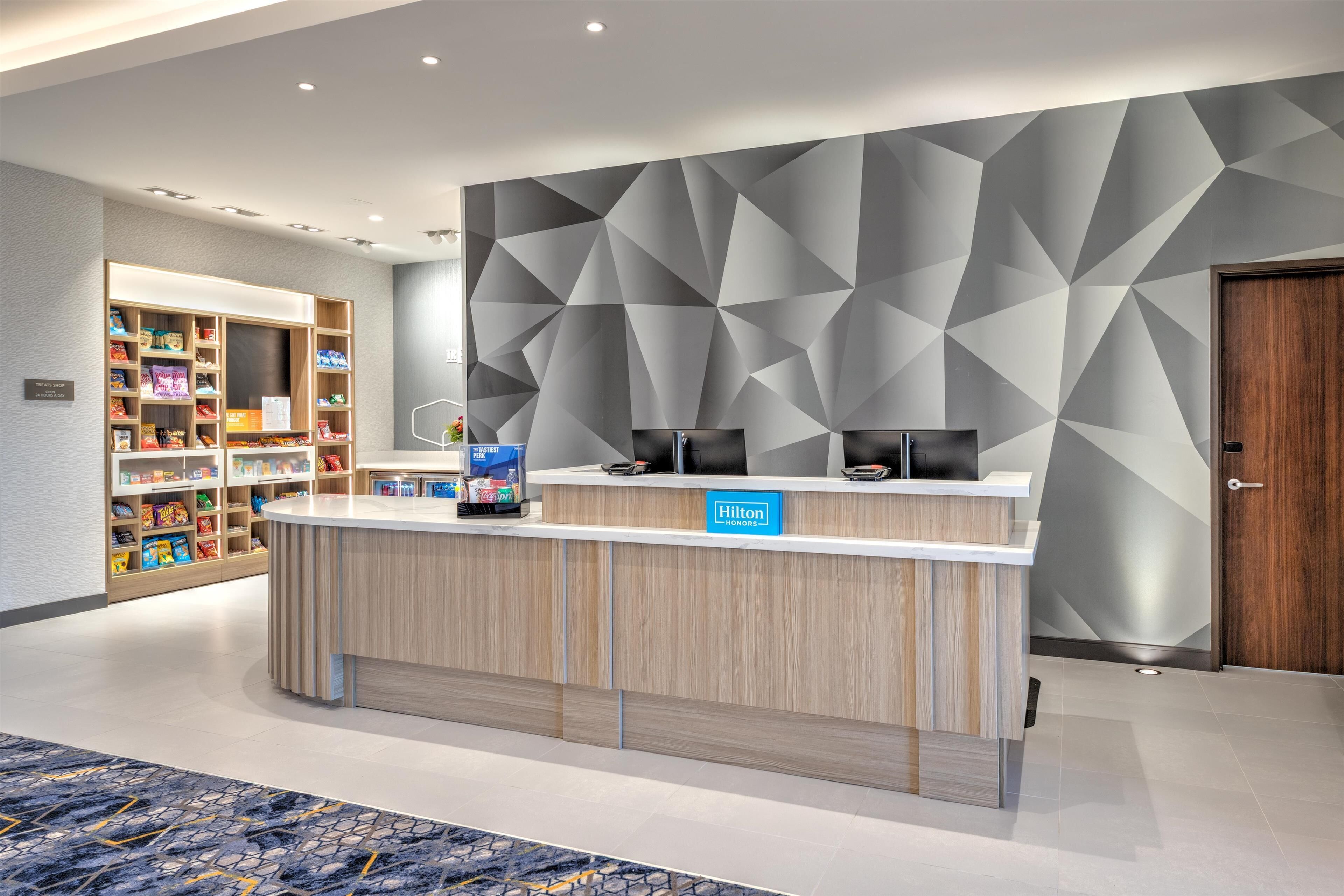 A hotel reception area with a modern design, featuring a wooden reception desk, a digital screen, and a wall with geometric patterns.