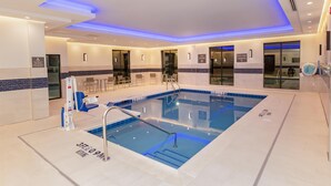 A modern indoor swimming pool with clear water, a diving board, and a seating area with chairs. - Hampton Inn & Suites Irving Hwy 183 (Irving)