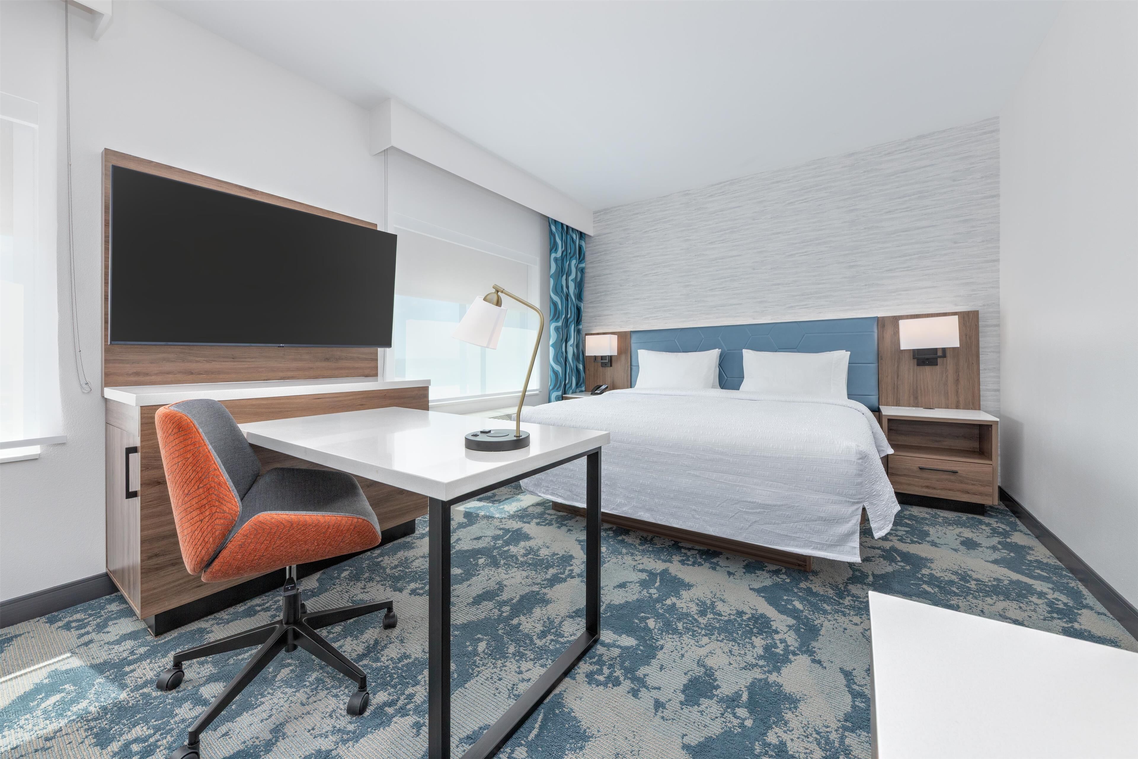 Habitación de hotel con cama, escritorio, silla y un televisor de pantalla plana grande.