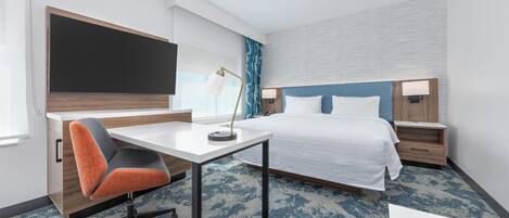 Habitación de hotel con cama, escritorio, silla y un televisor de pantalla plana grande.