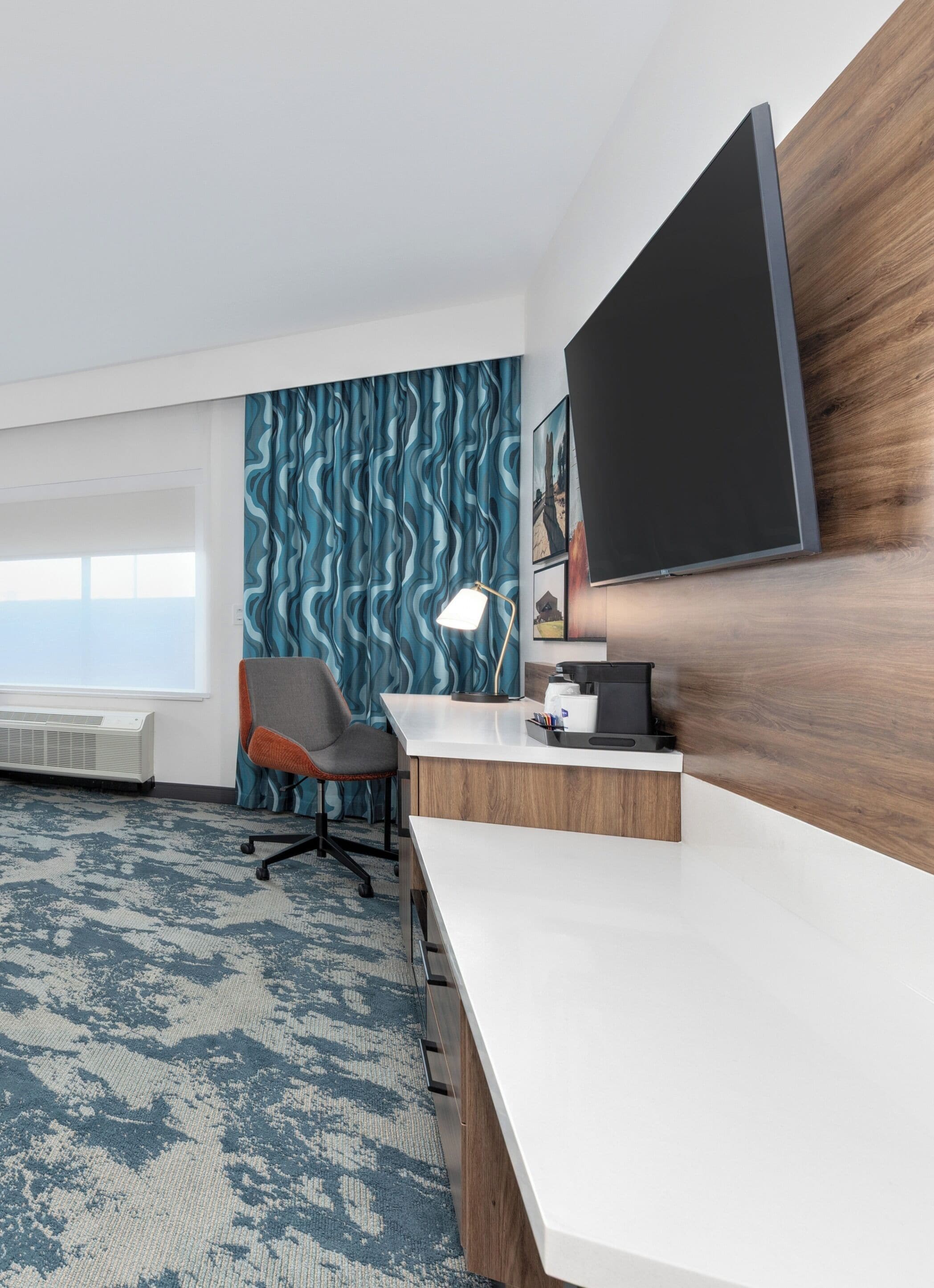 A modern office space with a white desk, a grey office chair, a large flat-screen TV, and a patterned wall.