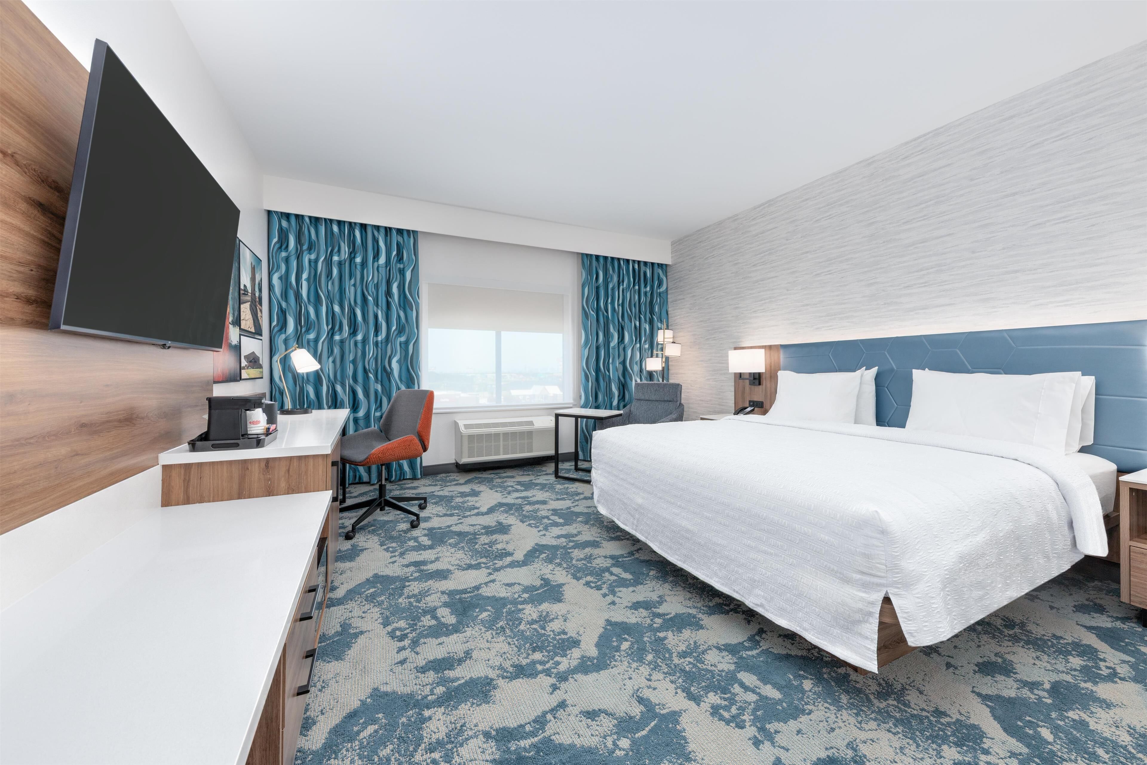 Une chambre d’hôtel avec un grand lit, un bureau avec une chaise, un téléviseur à écran plat et une fenêtre avec des rideaux.