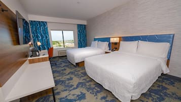 A hotel room with two beds, a desk, a mirror, and a window with a view.