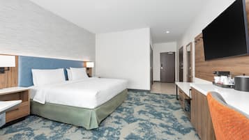 A modern hotel room with a bed, a desk, a flat-screen TV, and a bathroom visible through an open door.