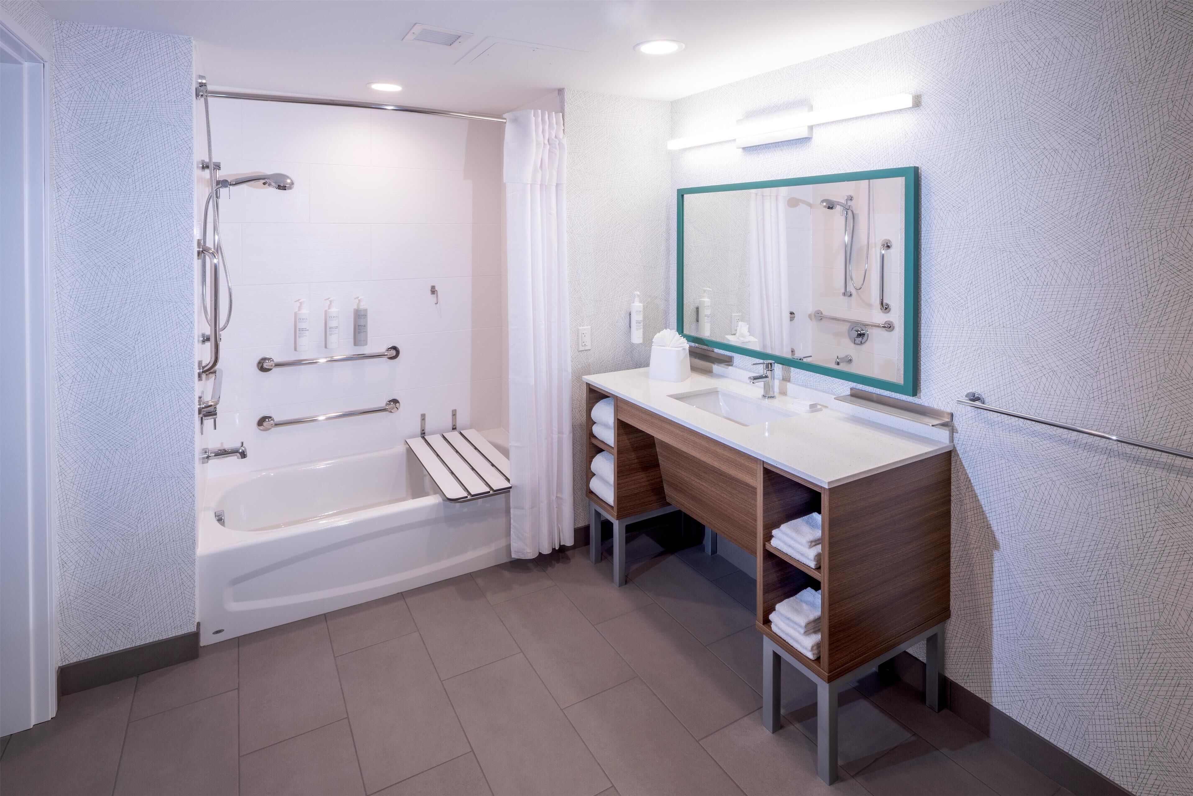 A modern bathroom with a bathtub, shower, vanity, and a large mirror.