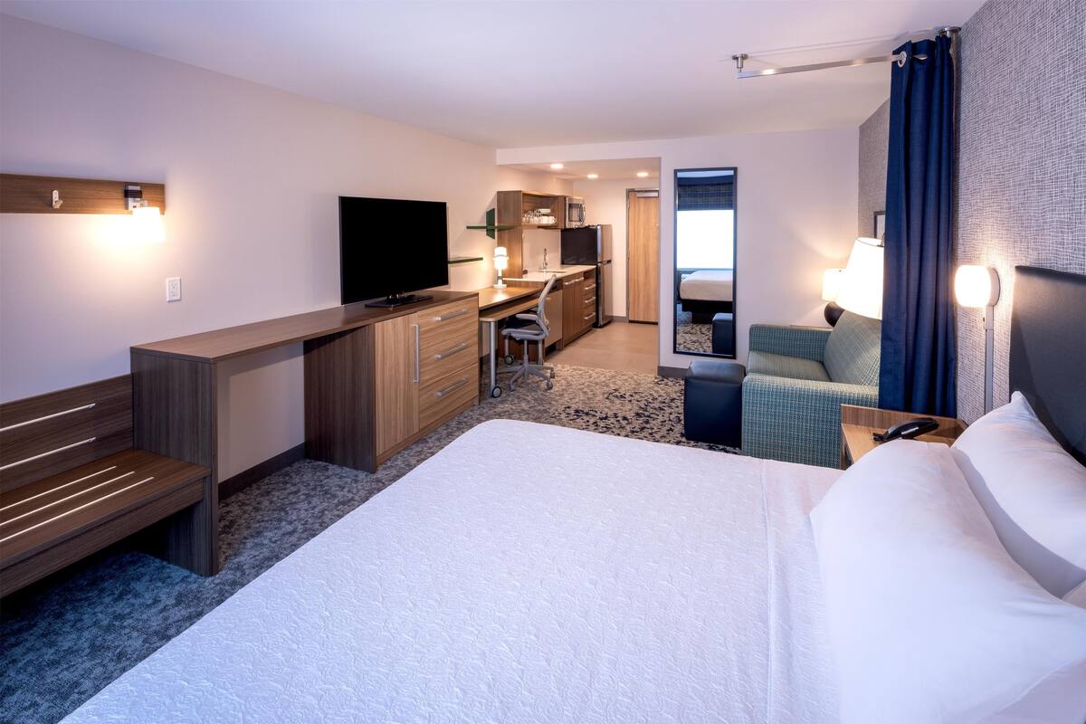 A hotel room with a bed, desk, chair, television, and a small kitchenette.