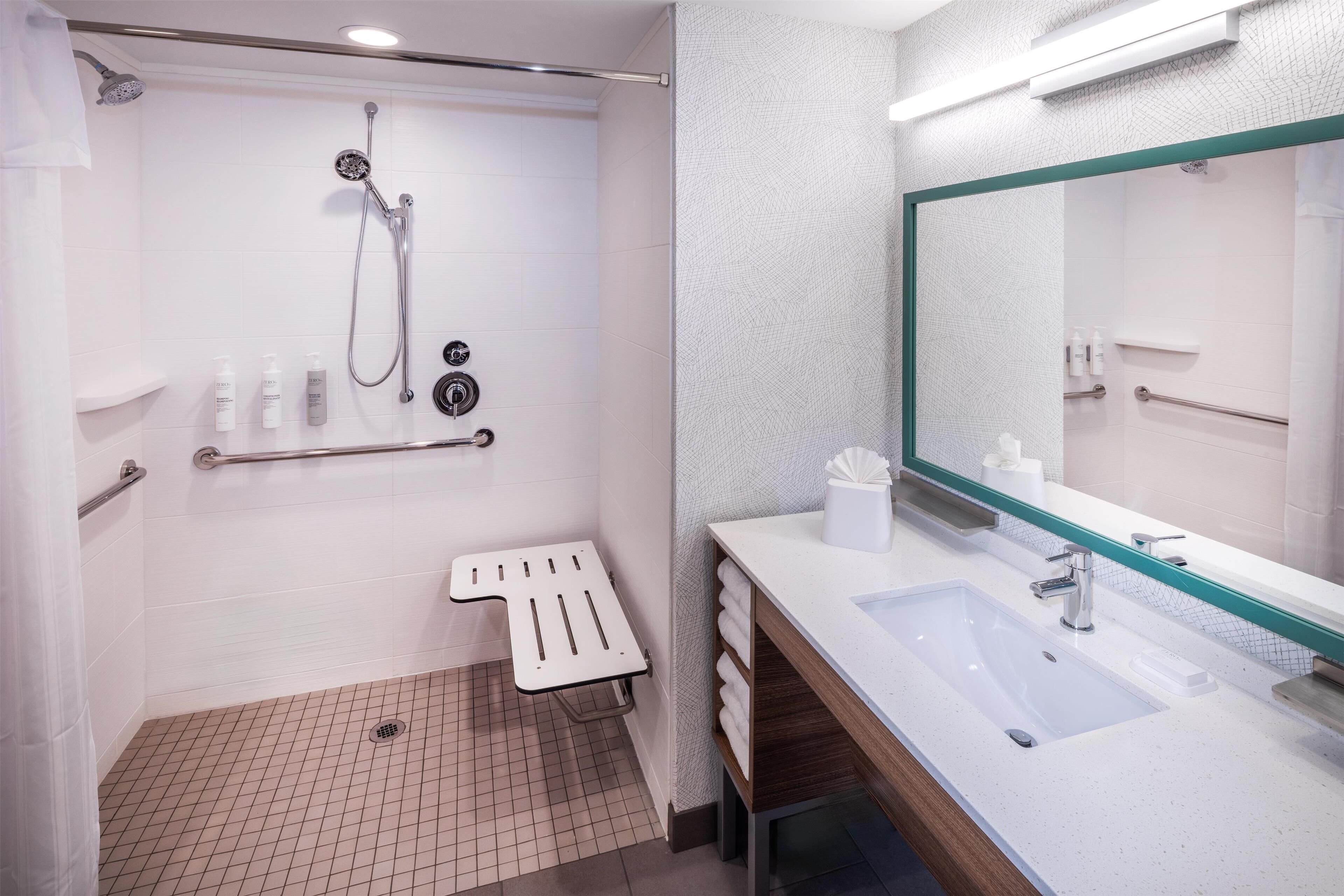 Une salle de bain moderne équipée d’une douche, d’une barre d’appui et d’un lavabo avec un miroir.
