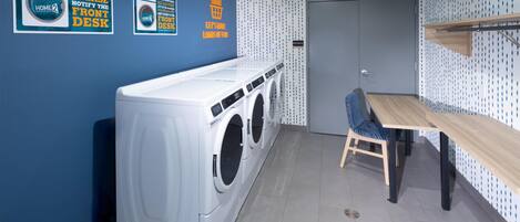 Une buanderie équipée d’un lave-linge, d’un étendoir et d’une table avec des chaises. Il y a des panneaux sur le mur et une porte avec une poignée.