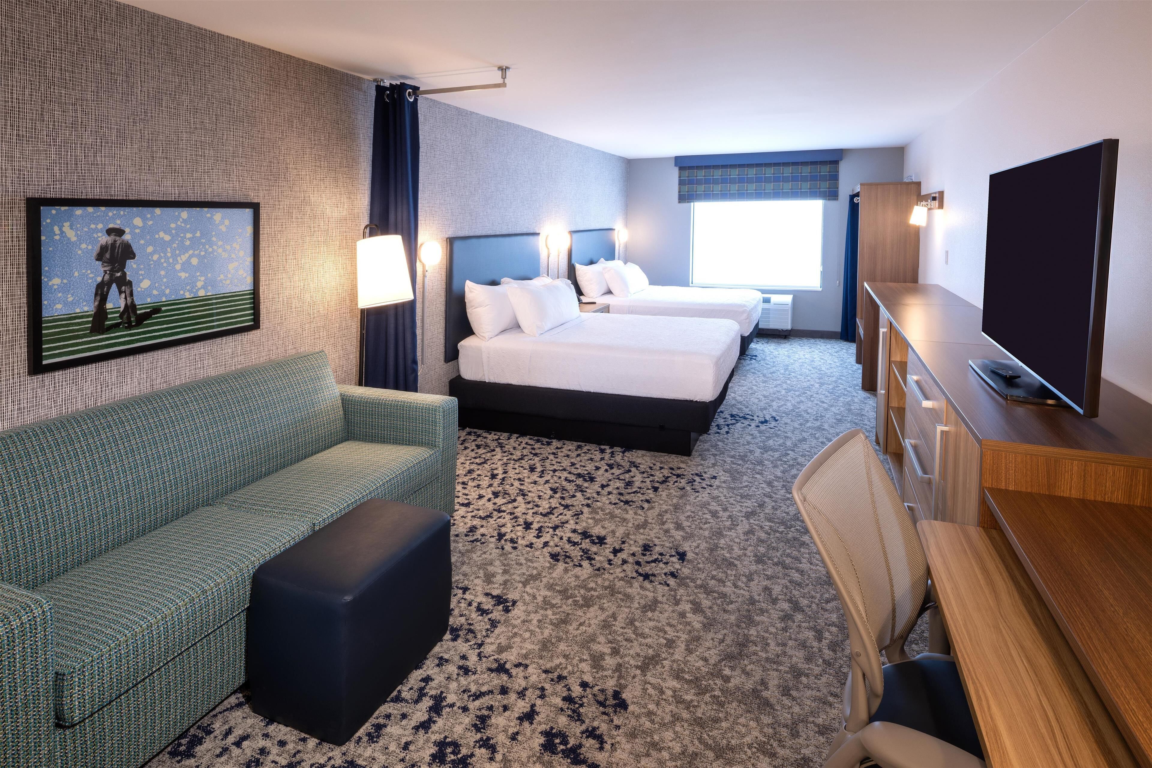 Habitación de hotel con dos camas, un sofá, un televisor y un escritorio.