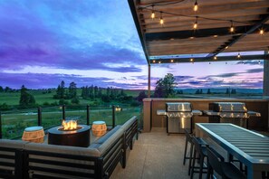 An outdoor patio with a fire pit, seating, and grilling stations, overlooking a scenic landscape. - Home2 Suites by Hilton Kalispell Whitefish (Kalispell)