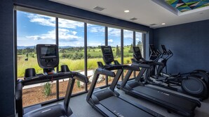 Ein Fitnessraum mit Laufbändern und Crosstrainern, große Fenster mit Blick auf eine grüne Landschaft.