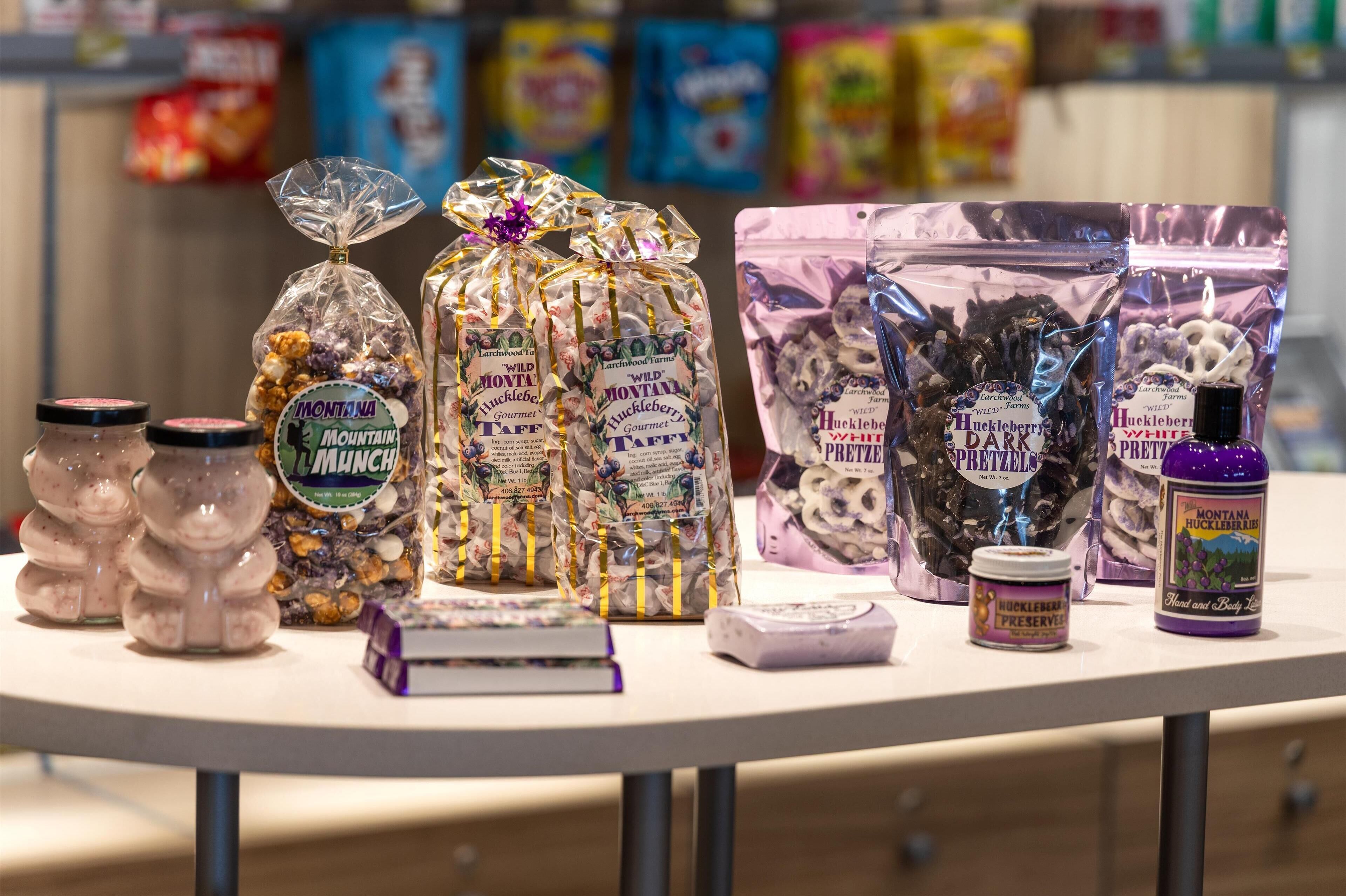 Exposição de diversos petiscos e conservas, incluindo Mountain Munch, Wild Monty Taff e Pretzels de Mountain Huckleberry, sobre uma mesa em uma loja.