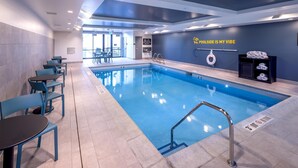 Ein Hallenbad mit blauen Stühlen und Tischen, einem Rettungsring und einem Schild mit der Aufschrift 'POOLSIDE IS MY VIBE'.