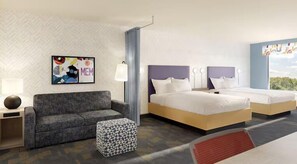 A hotel room with a sofa, two beds, a patterned ottoman, a wall art piece, and a window with a view.