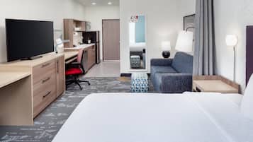 Una habitación de hotel con cama, escritorio, televisor, silla, sofá y lámpara.