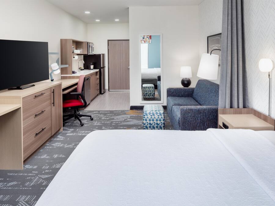 Una habitación de hotel con cama, escritorio, televisor, silla, sofá y lámpara.