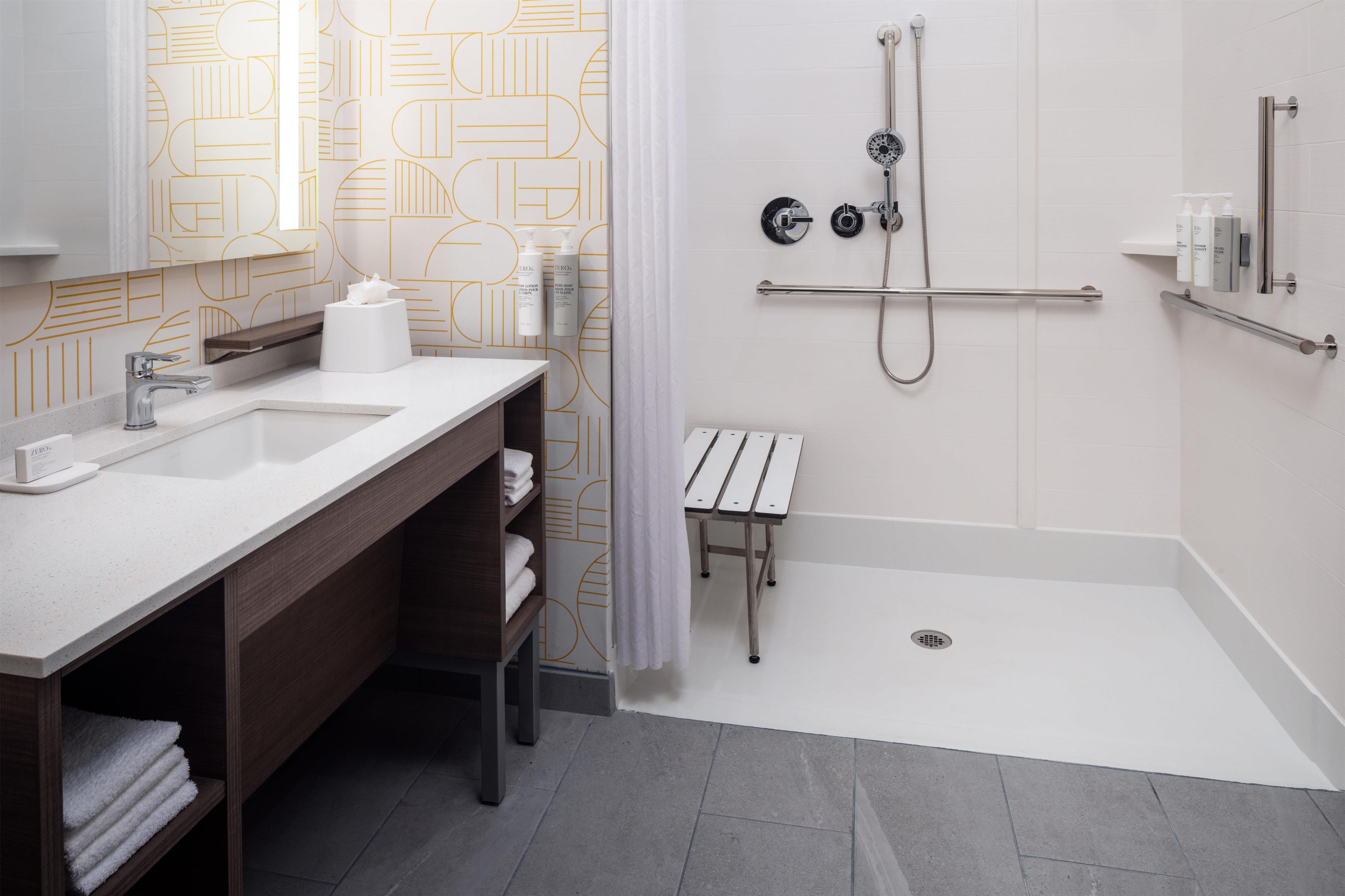 A modern bathroom with a dual sink vanity, a shower with a handheld showerhead, and a small bench.
