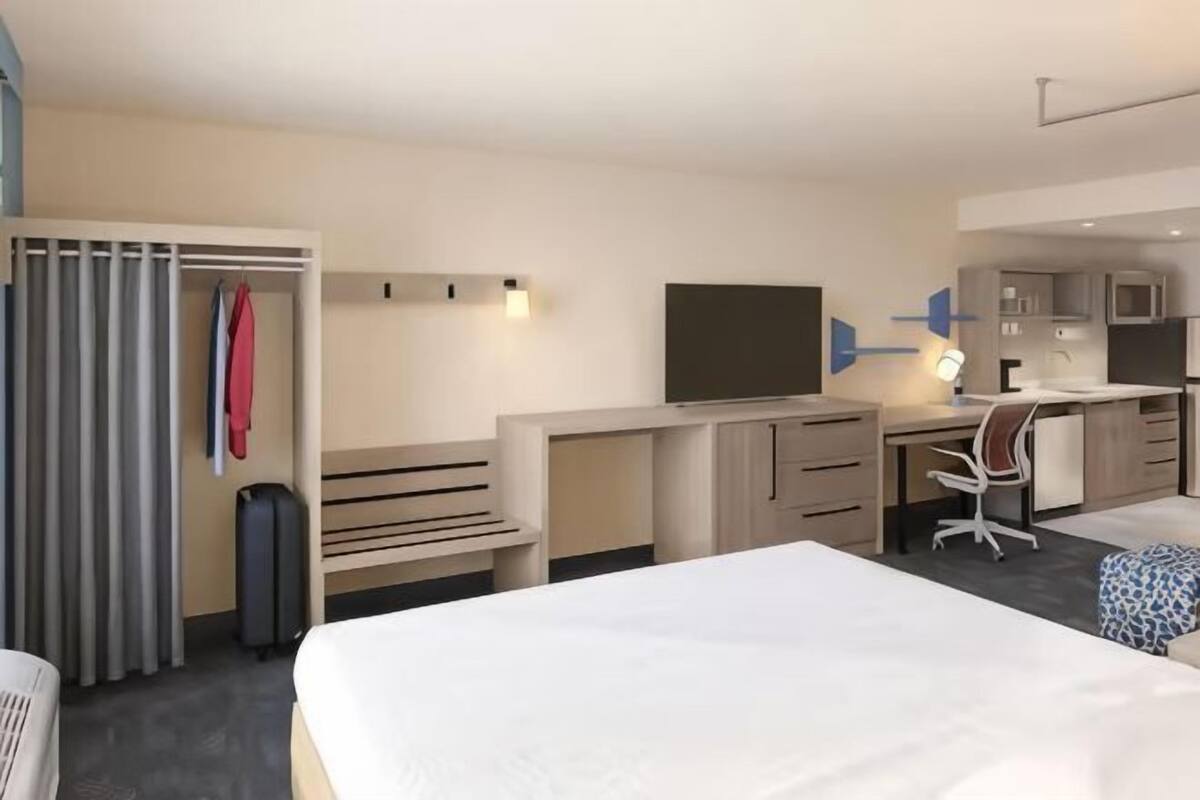 A hotel room with a bed, desk, chair, TV, and a wardrobe.