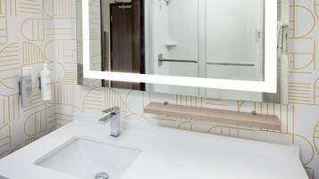 A bathroom with a large mirror, a white sink, and a shower area.