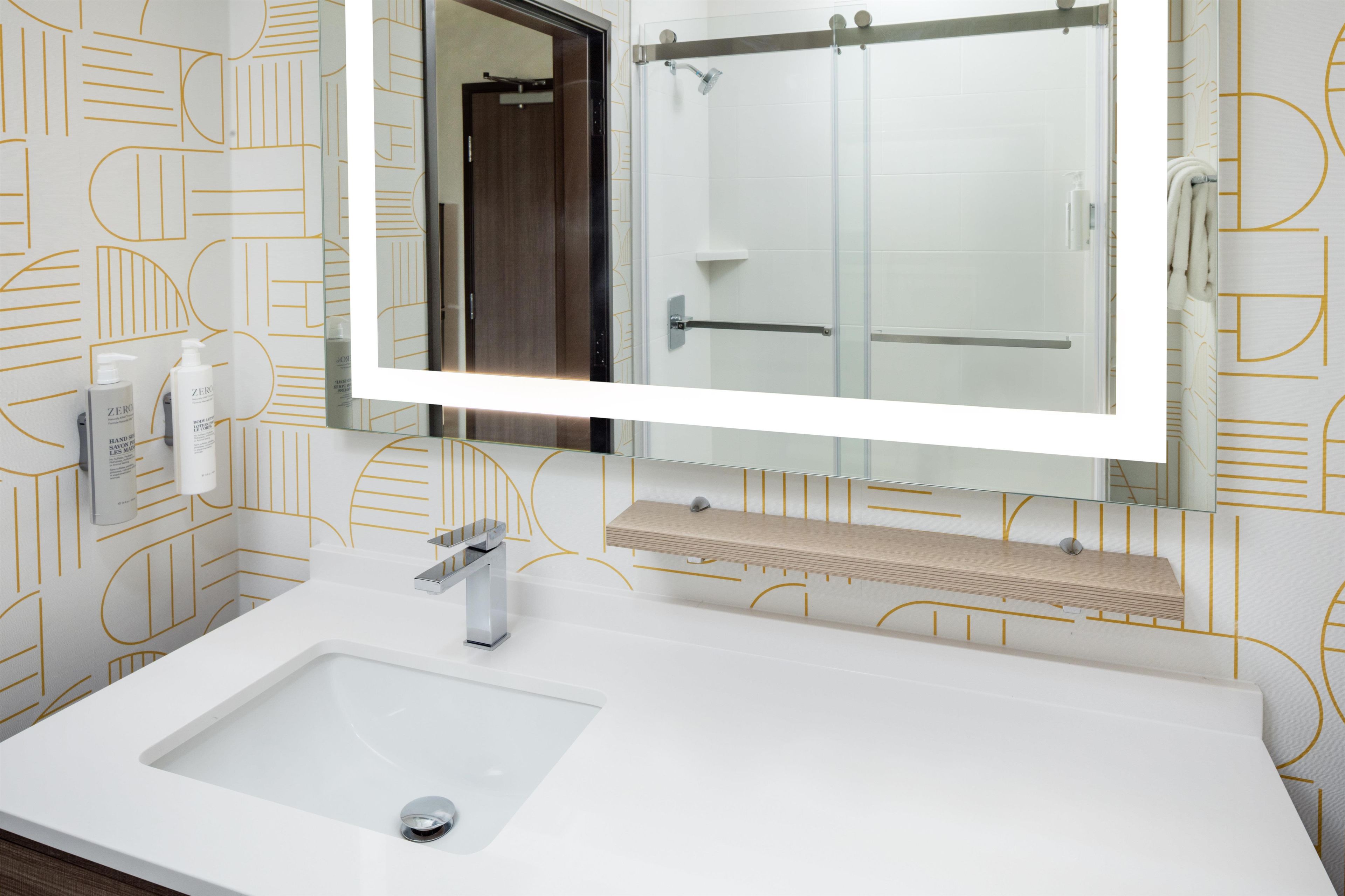 Une salle de bain avec un grand miroir, un lavabo blanc et un espace douche.
