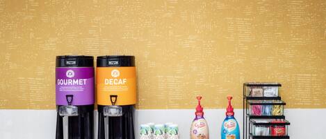 Two coffee dispensers labeled 'GOURMET' and 'DECAF' with stacks of disposable cups beside them.