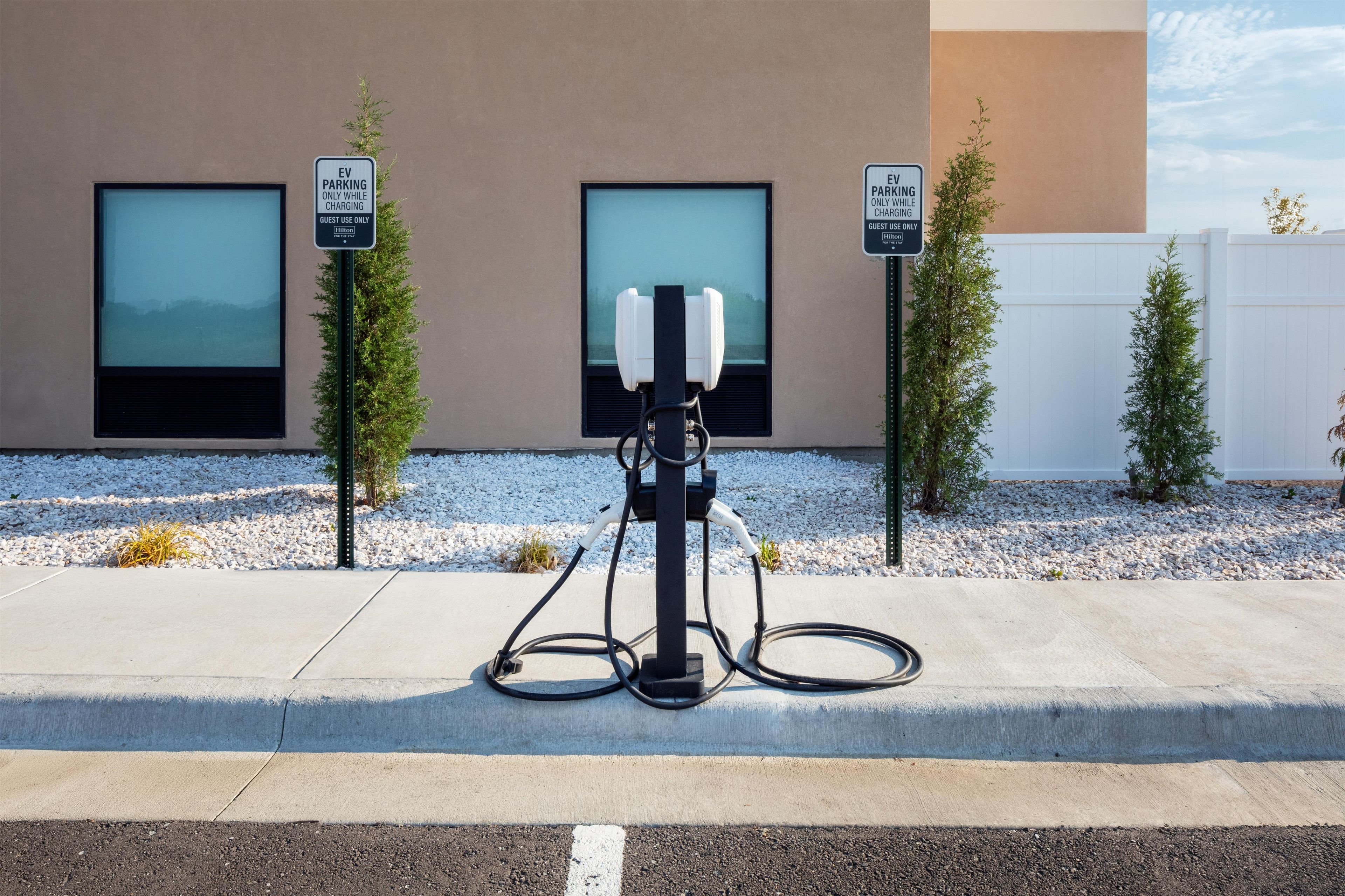 Una estación de carga para vehículos eléctricos con dos letreros que indican uso exclusivo para huéspedes de Hilton.