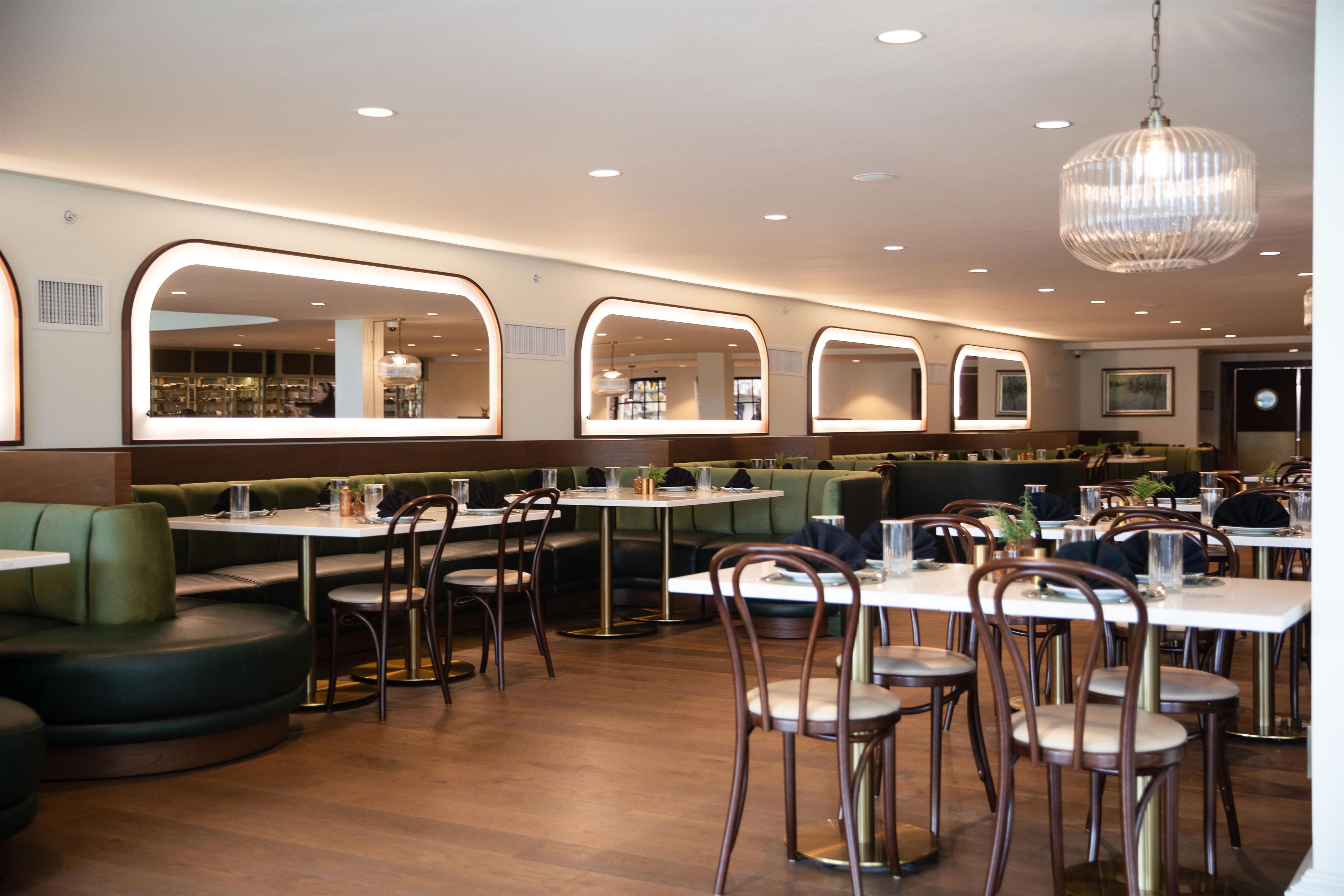 A restaurant with booths and tables, wooden flooring, and pendant lighting.