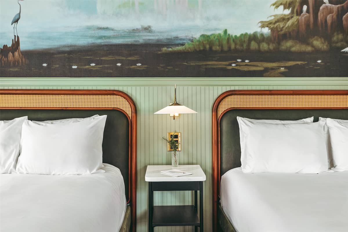 Una habitación de hotel con dos camas, una mesita con una lámpara y un mural en la pared.