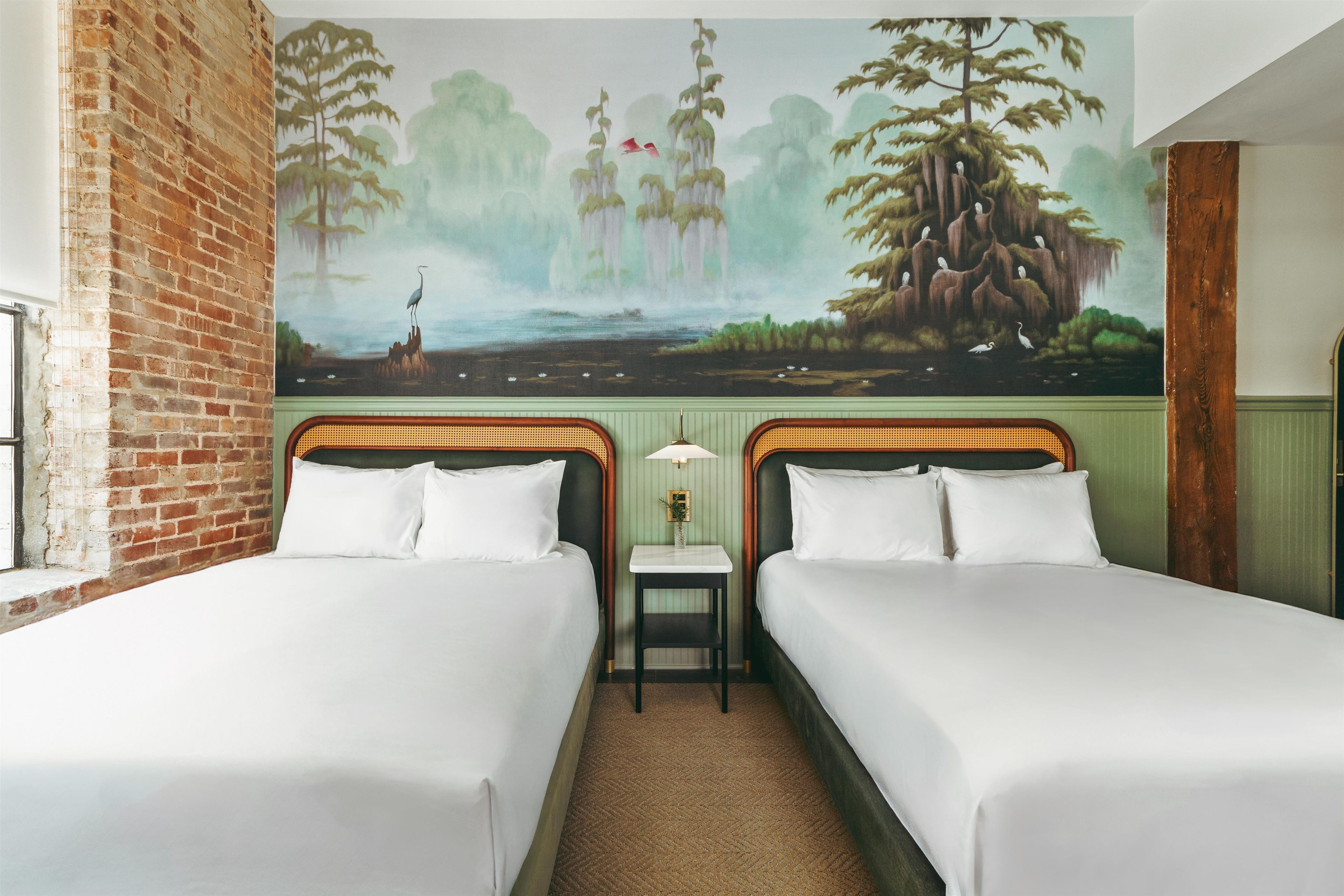 A hotel room with two beds, a mural of a forest scene, a brick wall, and a wooden headboard.