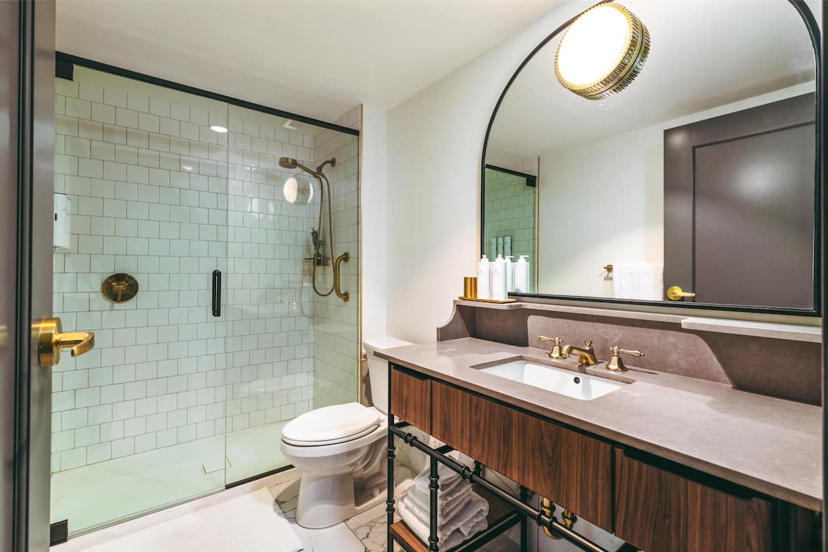 Un baño moderno con ducha envuelta en vidrio, inodoro blanco, tocador con lavabo y espejo, y un perchero para toallas.