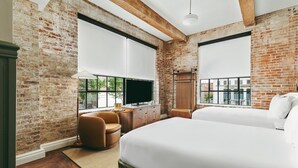 A hotel room with exposed brick walls, large windows, a bed, a desk with a TV, and a chair. - The Hotel Monroe, Tapestry Collection By Hilton (Monroe)