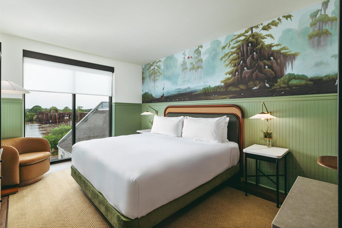 Habitación de hotel con una cama grande, una silla, una mesita y un mural en la pared.