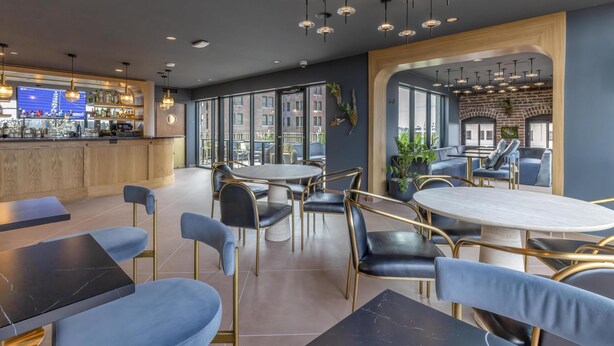 A modern interior with round tables and chairs, a bar area, and large windows offering views of the city. - The Hotel Monroe, Tapestry Collection By Hilton (Monroe)