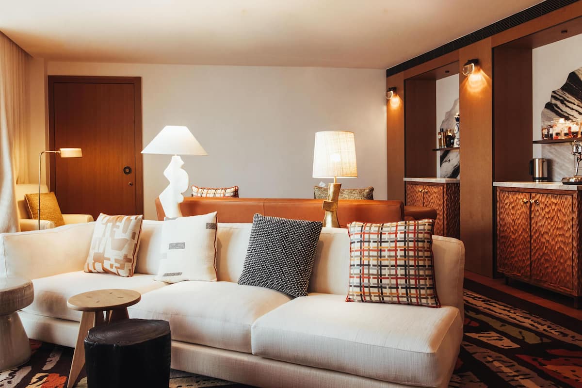 Hotellihuone, jossa on sohva, kaksi lamppua, pieni pöytä, kuvioitu matto ja minibaari.