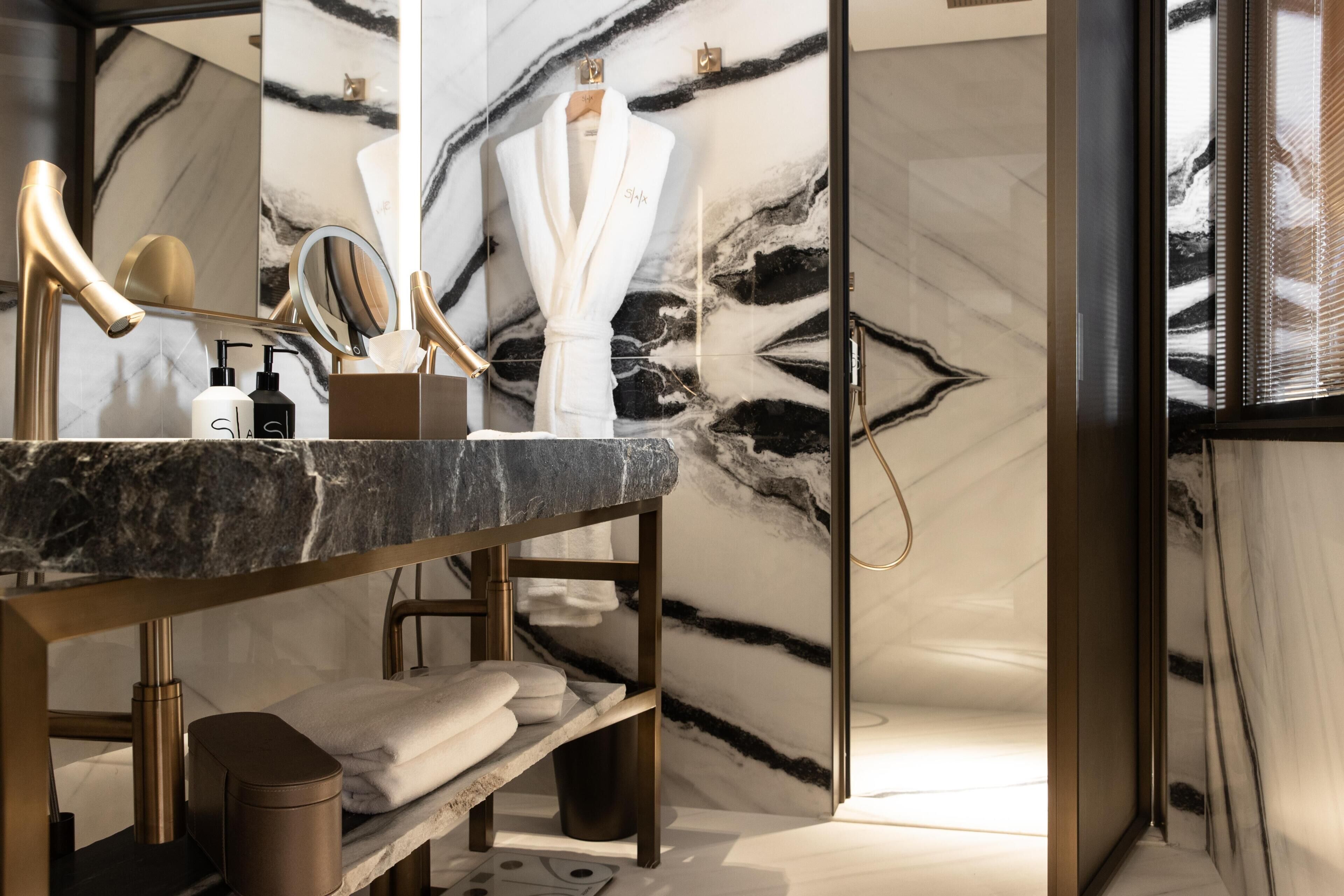 Ein modernes Badezimmer mit Marmorwaschtisch, goldenen Armaturen und einem an der Wand hängenden Bademantel.