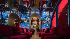En lyxig inredning med röda sammetsklädda sittplatser, en stor kristallkrona i taket och en spegelvägg som reflekterar en skogsmiljö.